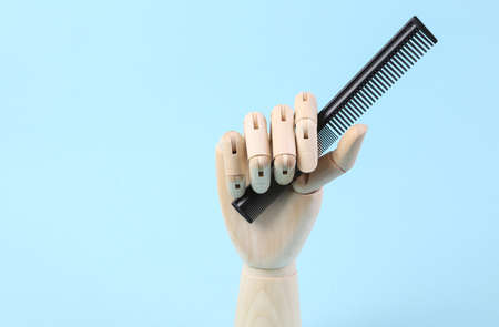Wooden hand holds comb on blue background