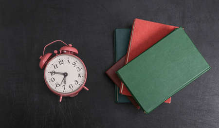 alarm clock and stack of books on blackboardの写真素材
