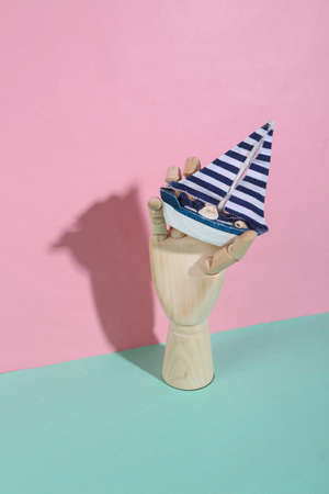 Wooden hand holding boat on blue pink pastel background. trendy shadow. concept art. minimalism. creative layoutの写真素材