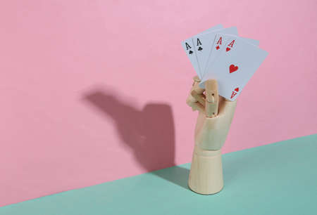Wooden hand holding four aces on blue pink pastel background. trendy shadow. concept art....