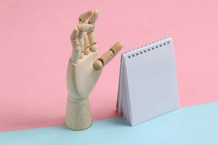 Notebook and wooden hand stands on blue-pink pastel background. minimalismの写真素材