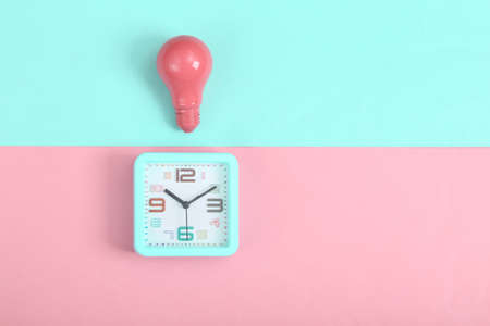 Alarm clock and pink light bulb on pink blue background. minimalism. top view
