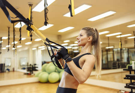 Young fit woman trains with trx resistance belts in the fitness gym. healthy lifestyle. bodyweight...
