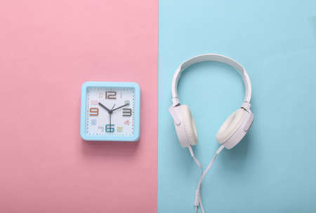 Square alarm clock with headphones on pink blue background. music time. top viewの写真素材