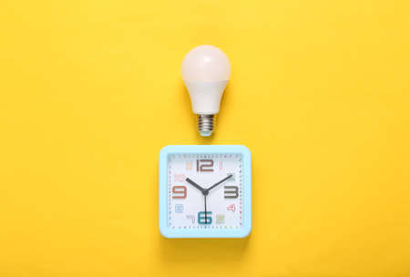 Alarm clock and light bulb on yellow background. top viewの写真素材