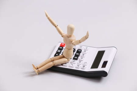 Happy wooden puppet sitting on calculator on gray backgroundの写真素材