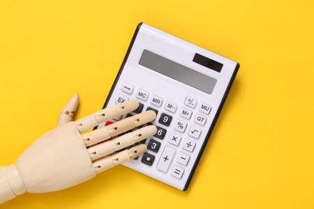 Wooden hand using calculator on yellow backgroundの写真素材