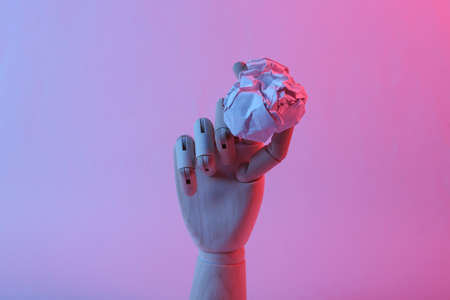 Wooden hand holding crumpled paper ball in pink blue gradient neon lightの写真素材