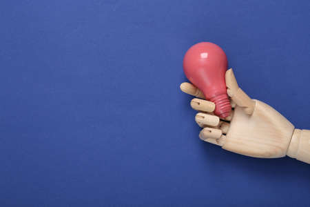 Wooden hand holding pink light bulb on blue backgroundの写真素材