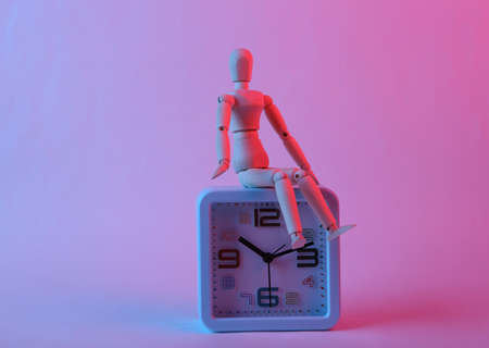 alarm clock with wooden puppet in pink blue gradient neon lightの写真素材