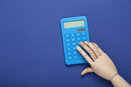 Wooden hand uses a calculator on blue backgroundの写真素材