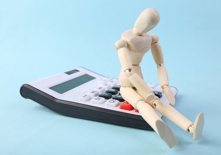 Sad wooden puppet and calculator on blue backgroundの写真素材