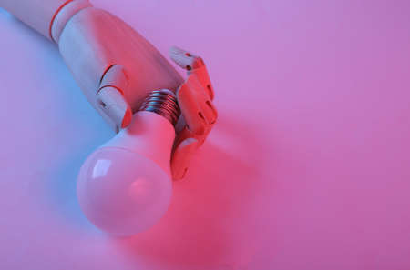 Wooden hand holding light bulb in pink blue gradient neon lightの写真素材