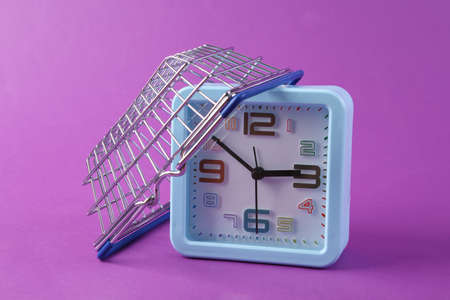 Clock with a shopping basket on purple background. shopping timeの写真素材