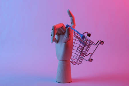 Wooden hand holding shopping trolley in pink blue gradient neon light