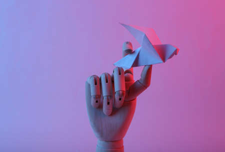 Wooden hand holding origami dove in pink blue gradient neon lightの写真素材
