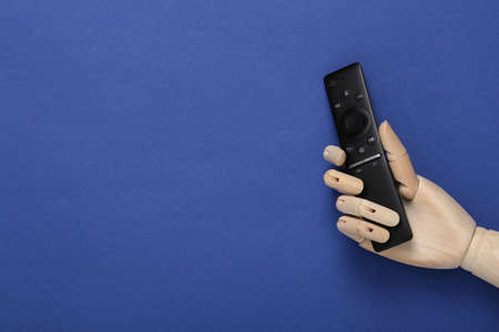 Wooden hand holding tv remote on blue background