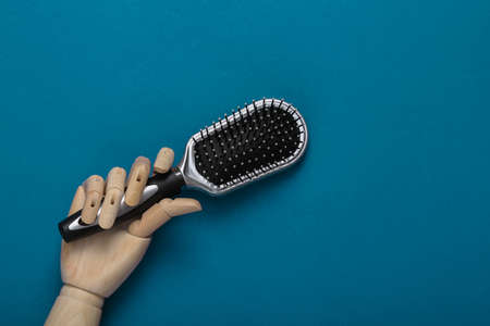 Wooden hand holding hair brush on blue background