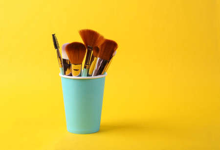 Makeup brushes in cup on a yellow background