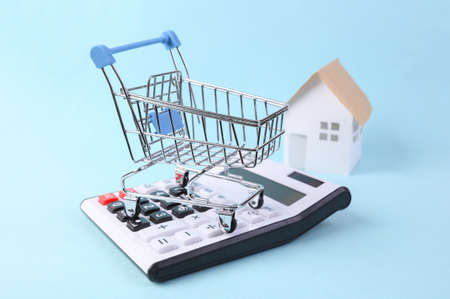 Shopping cart with calculator and model house on a blue background. home buying concept