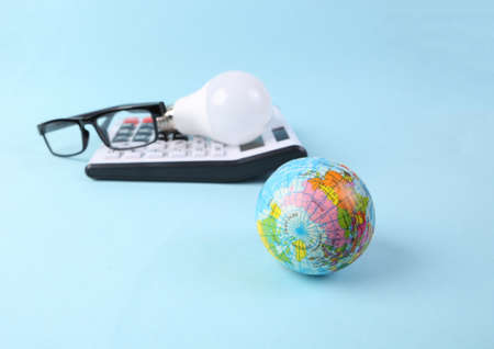 Eco concept. Globe, light bulb and calculator with glasses on a blue background. Electricity costsの写真素材
