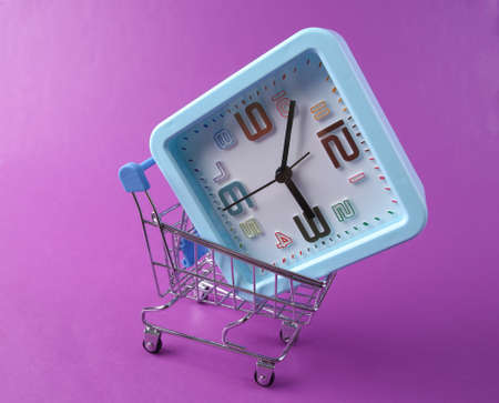 Clock with shopping trolley on purple background. shopping timeの写真素材