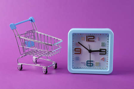 Clock with shopping trolley on purple background. shopping time