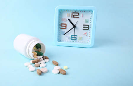 Bottle of pills and alarm clock on a blue background. Time to take pills