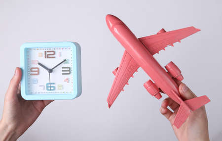 Hands holding alarm clock and plane on white background. Travel time