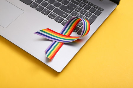 Laptop and LGBT rainbow ribbon pride tape symbol on yellow background. love concept
