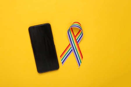 LGBT rainbow ribbon pride tape symbol with smartphone on yellow background.