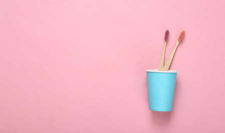 Two eco bamboo toothbrushes in cardboard cup on pink backgroundの写真素材