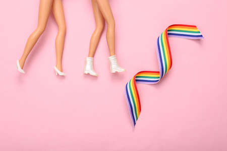 Lgbt community, lesbian relationship concept. Dolls feet and rainbow lgbt symbol ribbon on pink...