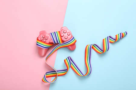 Gamepad with LGBT rainbow ribbon tape on blue pink background.
