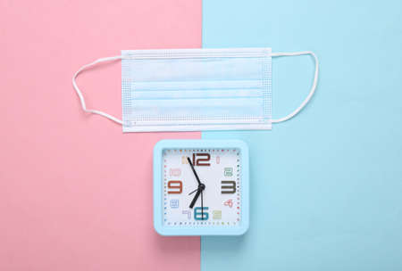 Medical mask and alarm clock on pink blue background