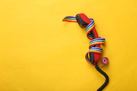 Phone tube and LGBT rainbow ribbon pride tape symbol on yellow background.