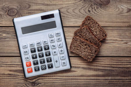 Calculator with Sliced whole grain rye bread on wooden background. Diet, calorie counting conceptの写真素材
