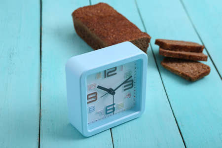 Alarm clock with Sliced whole grain rye bread on blue wooden background.