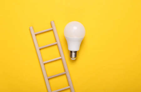 Wooden staircase and light bulb on yellow background. Motivation, idea conceptの写真素材