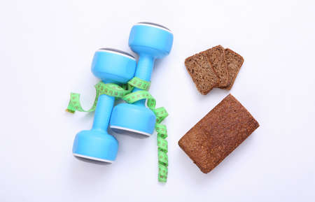 Measuring tape and dumbbells, diet whole grain rye bread on a white background. Weight loss, diet,...