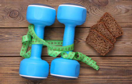 Measuring tape and dumbbells, diet whole grain rye bread on wooden background. Weight loss, diet, fitness conceptの写真素材