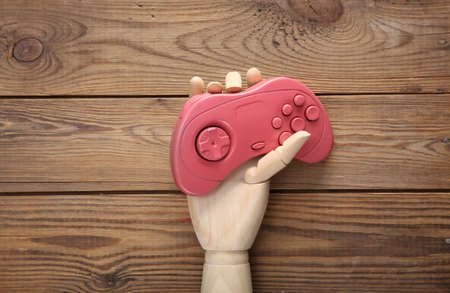 Wooden hand holds pink gamepad on wooden background