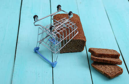 Shopping trolley with Sliced whole grain rye bread on blue wooden background