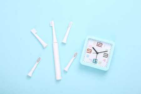 Ultrasonic plastic toothbrush with replaceable heads and alarm clock on blue background. Dental care...