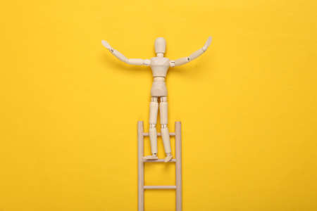 Wooden puppet climbs up the stairs on yellow background. career growth conceptの写真素材