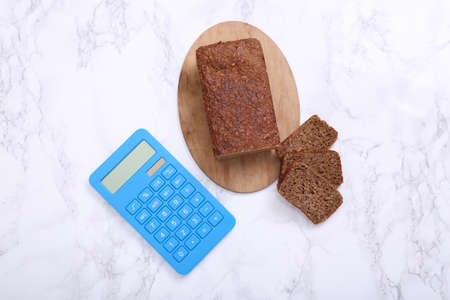 Calculator with Sliced whole grain rye bread on marble background. Diet, calorie counting concept
