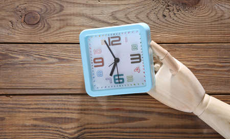 Wooden hand holds alarm clock on wooden background