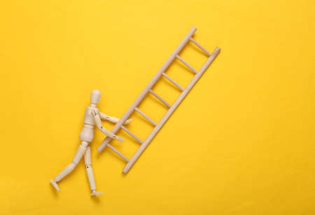Wooden puppet holding stairs on yellow background. career growth conceptの写真素材