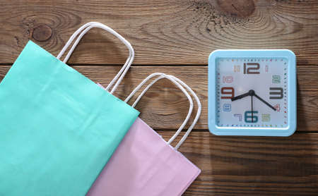 Alarm clock with shopping bag on wooden background. top view