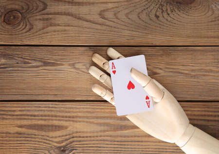 Wooden hand holding ace of hearts on wooden backgroundの写真素材